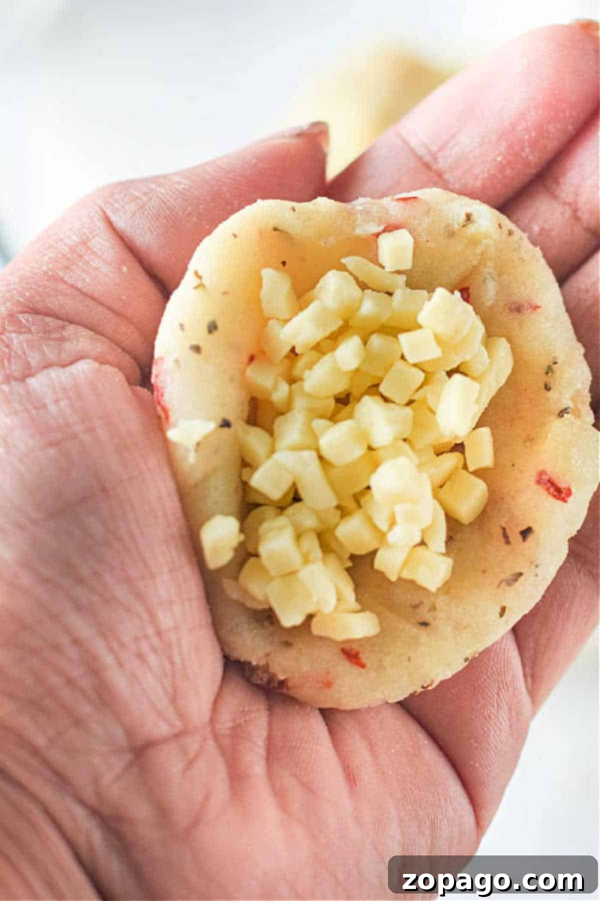 Crispy Air-Fried Mashed Potato Bites 5 A hand holds mashed potatoes filled with small cubes of cheese, ready to be formed into balls.