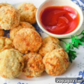Crispy Air-Fried Mashed Potato Bites 8 A plate of golden air fryer mashed potato balls with a bowl of red sauce, garnished with parsley on a blue and white floral plate.