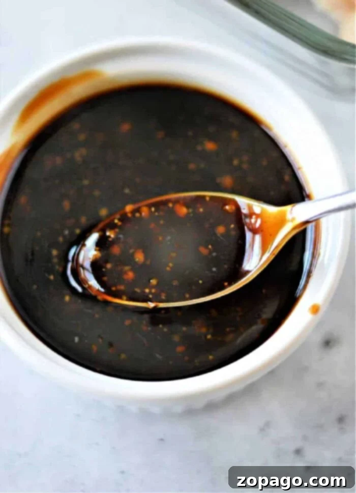 Crafting Perfect Homemade Teriyaki 2 A spoon dipped in a bowl of dark teriyaki sauce with specks of seasoning, reminiscent of how to make homemade teriyaki sauce, rests on a white surface.