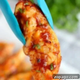 Guilt-Free Air Fryer Chicken 9 Close-up of grilled BBQ chicken held by blue tongs, garnished with herbs. This air fryer chicken recipe requires no breading, highlighting the perfect blend of smokiness and freshness.
