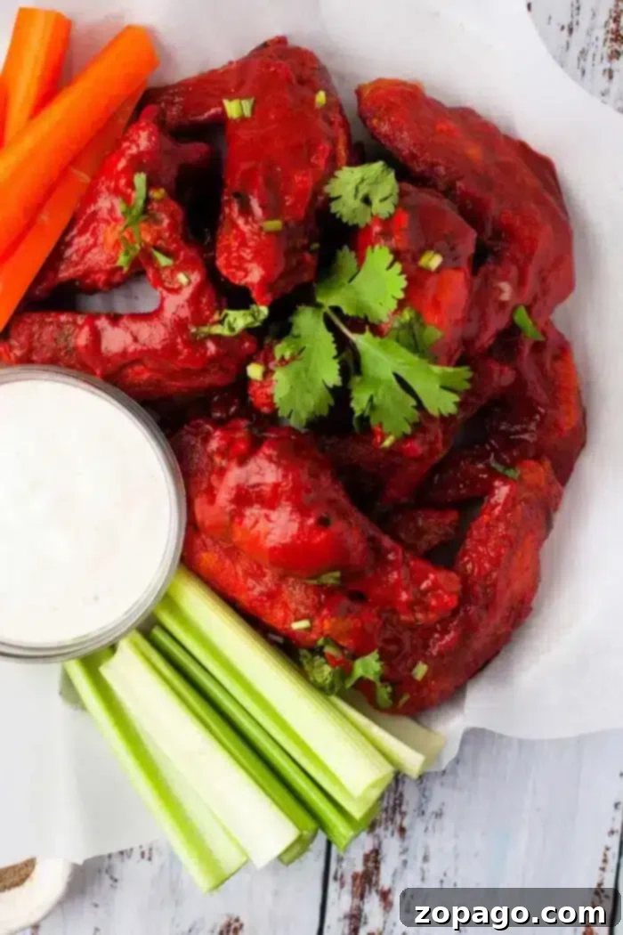 Crispy Ninja Foodi Air Fryer BBQ Chicken Wings 2 A plate of saucy buffalo chicken wings, cooked to perfection in an air fryer, garnished with cilantro, served with carrot and celery sticks, and a small cup of white dipping sauce on the side. The food is presented on parchment paper.