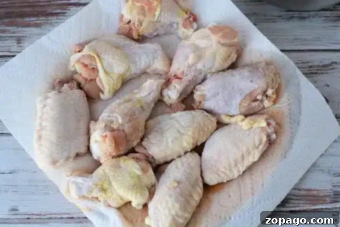 Crispy Air Fryer Chicken Wings with Baking Powder 4 Raw chicken wings and drumsticks laid out on a white paper towel on a rustic wooden table, preparing for seasoning and air frying with baking powder for extra crispiness.