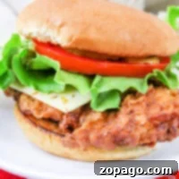 An air fryer gives this crispy chicken sandwich its perfectly golden finish. Topped with lettuce, tomato, and cheese on a soft bun, it's reminiscent of a classic McDonald's favorite and served on a white plate.