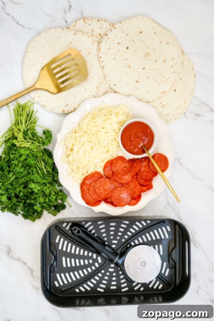 Effortless Air Fryer Tortilla Pizzas 3 Air Fryer Tortilla Pizza essentials: tortillas, shredded cheese, pepperoni, sauce, parsley, spatula, pizza cutter, and an air fryer basket arranged on the counter, ready for assembly.