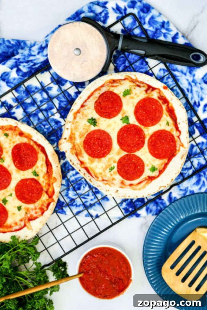 Effortless Air Fryer Tortilla Pizzas 6 Two Air Fryer Tortilla Pizzas resting on a cooling rack, accompanied by a pizza cutter, a bowl of sauce, and utensils, ready for serving.