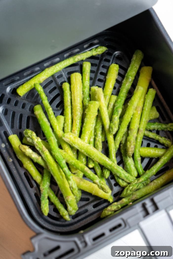 Easy Air Fryer Frozen Asparagus 4 Close-up of frozen asparagus spears arranged in a single layer in an air fryer basket, ready for cooking.