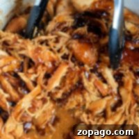 Frozen chicken thighs turn into tender, shredded barbecue goodness as theyre slow-cooked in a Crock Pot. The savory sauce melds perfectly, and when mixed with metal tongs in a white container, it becomes an irresistible delight.