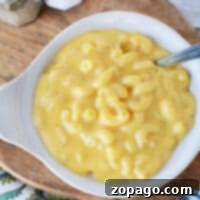A bowl of creamy microwave mac and cheese sits invitingly on a wooden board, complete with a spoon ready for tasting, nestled beside salt and pepper shakers.