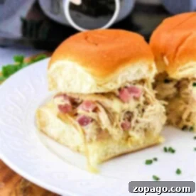 Pulled chicken sliders, reminiscent of a Chicken Cordon Bleu Sandwich, are topped with chopped onions and cheese on a white plate, elegantly presented on a wooden surface.