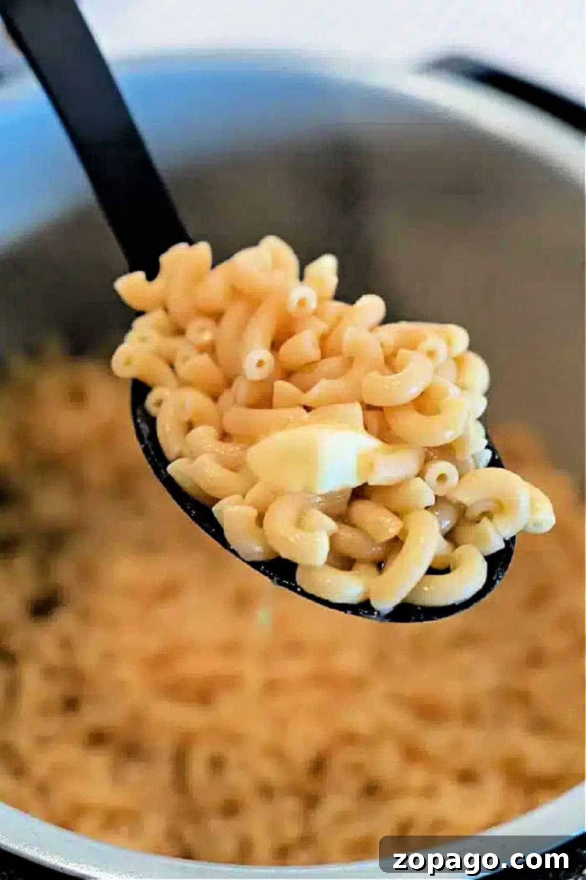 Ninja Foodi Garlic Butter Noodles 2 A spoonful of cooked elbow macaroni with a piece of butter, held over a pot of more macaroni—perfect for making creamy Ninja Foodi Butter Noodles.
