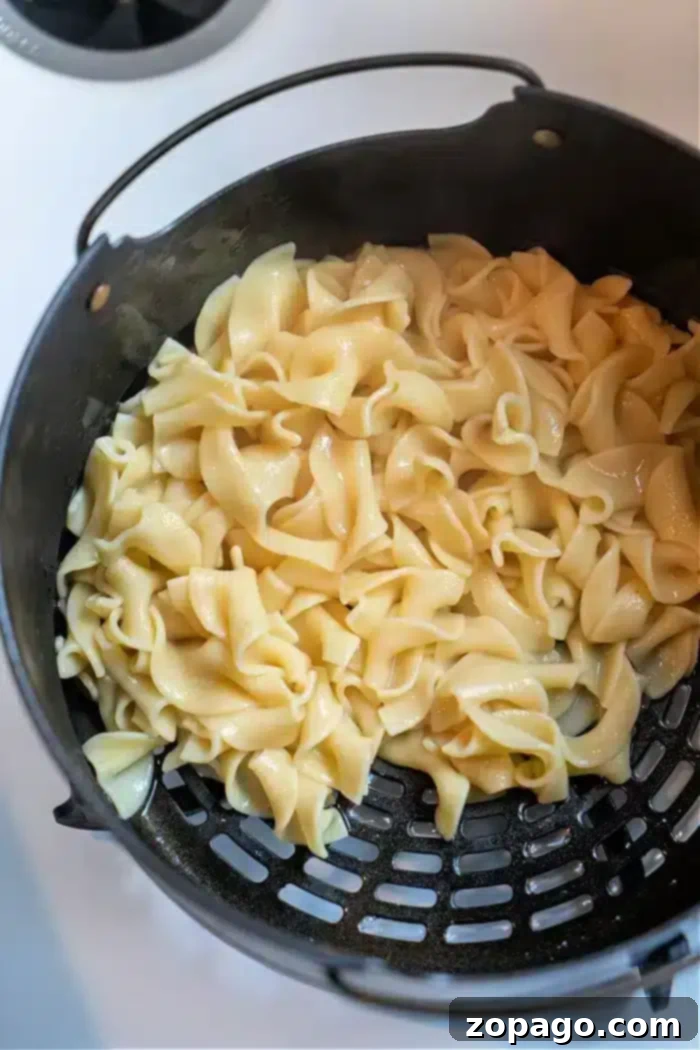 Ninja Foodi Garlic Butter Noodles 5 Cooked pasta noodles glisten in a black colander, showcasing their glossy texture from above. Their silky appearance suggests they've been transformed into delicious Ninja Foodi butter noodles, capturing the essence of creamy perfection as they rest in the strainer.