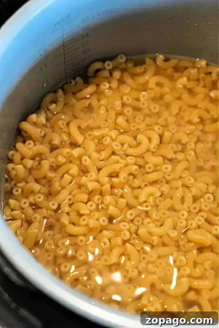 Ninja Foodi Garlic Butter Noodles 6 A pot filled with elbow macaroni pasta sits in water up to the 18-cup mark, perfect for making a delicious batch of Ninja Foodi butter noodles, indicating the pasta is being cooked or soaked.