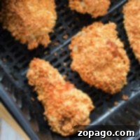Four pieces of crispy, golden-brown gluten-free chicken are arranged in an air fryer basket. The chicken appears evenly cooked and crunchy. The basket rests on a light-colored wooden surface.