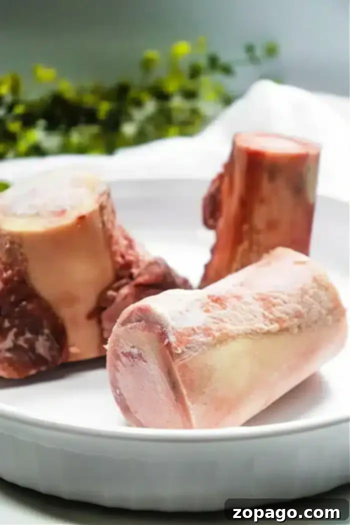Three raw beef bones, ideal for air frying, presented in a white dish with blurred green foliage in the background.