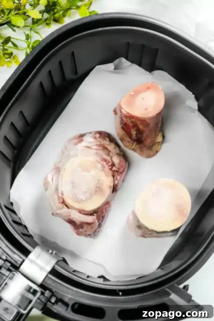 Juicy beef marrow bones resting on parchment paper in an air fryer basket, garnished with green leaves.