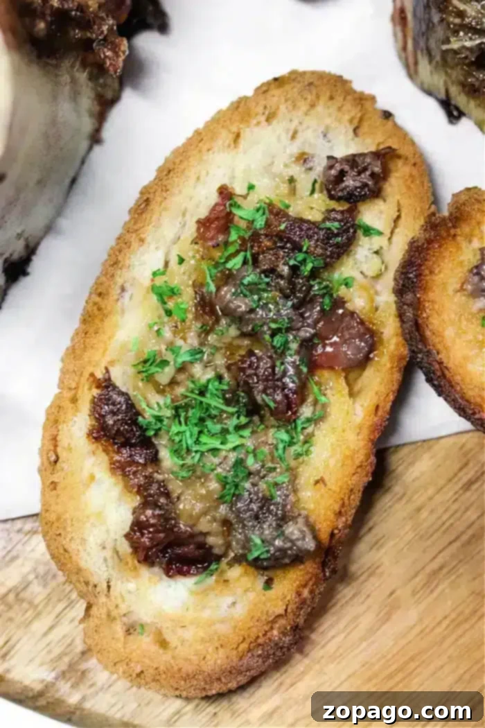 Air Fryer Roasted Bone Marrow 7 A slice of golden toasted bread, generously topped with savory bone marrow and garnished with fresh parsley, served on a rustic wooden surface.