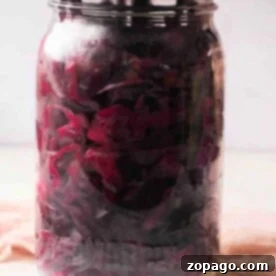 A jar of purple pickled cabbage with a metal lid rests on a light surface, showcasing the vibrant color and tangy aroma reminiscent of a classic pickled red cabbage recipe.