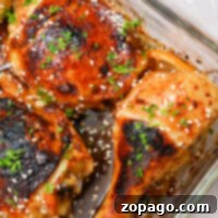 A glass baking dish features Teriyaki chicken drumsticks and thighs, garnished with sesame seeds and chopped herbs. The Cheesecake Factory-inspired chicken pieces are cooked to golden brown perfection with charred areas, and onion slices peek from underneath.