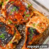 Easy Baked Teriyaki Chicken 7 A glass baking dish features Teriyaki chicken drumsticks and thighs, garnished with sesame seeds and chopped herbs. The Cheesecake Factory-inspired chicken pieces are cooked to golden brown perfection with charred areas, and onion slices peek from underneath.