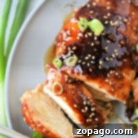Sliced teriyaki chicken breast on a plate, topped with sesame seeds and green onions, crafted from a simple teriyaki chicken recipe using bottled sauce, with a fork beside it.