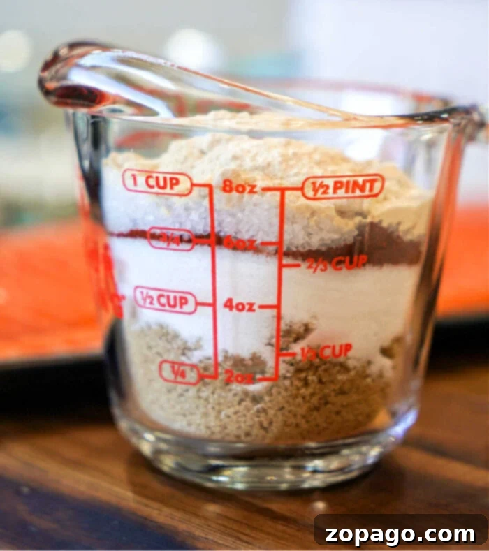 Ultimate Chicken Wing Dry Rub 2 A glass measuring cup filled with layered ingredients, perfect for crafting a dry rub for chicken wings, including white sugar, brown sugar, and cocoa powder. Red measurement lines indicate ounces, cups, and pints on its clear surface. It rests elegantly on a wooden countertop.