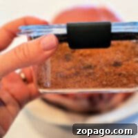 Unforgettable Homemade BBQ Rub 7 A hand holds a glass container filled with seasoned dry rub for pork chops, ready for barbecuing.