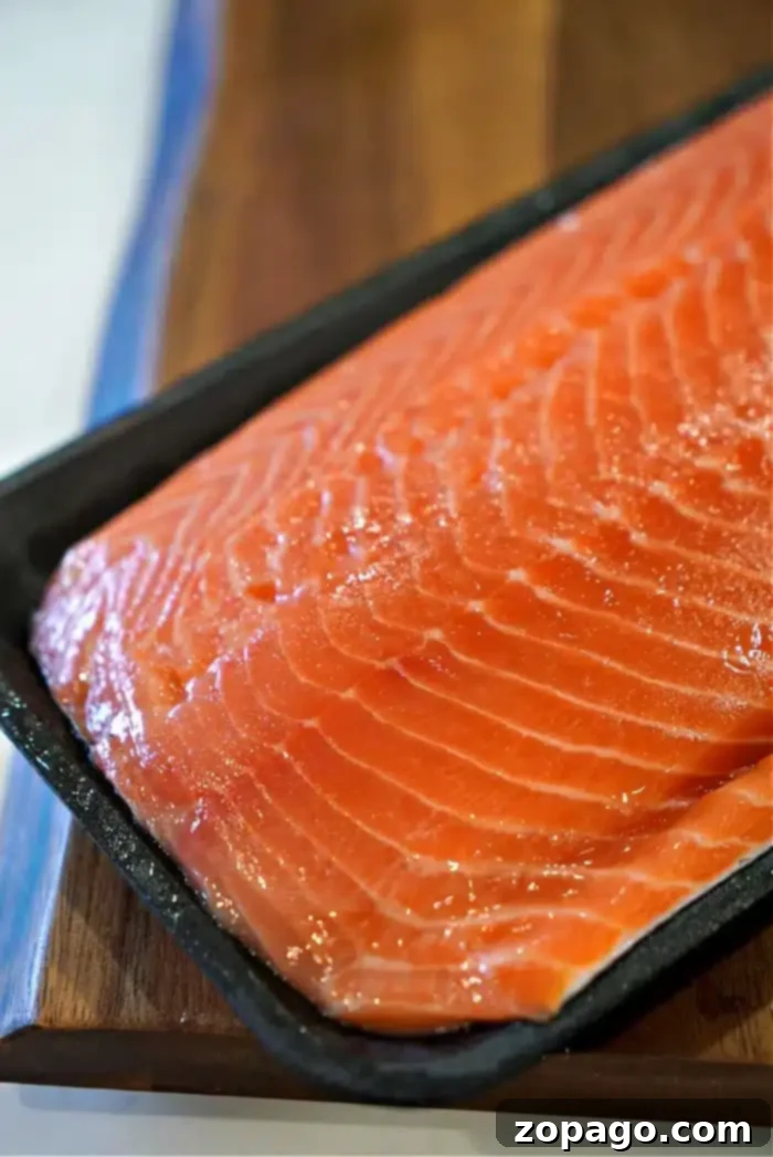 Sticky Teriyaki Salmon 3 A vibrant, fresh raw salmon fillet, showcasing its rich orange color and delicate marbling, prepared on a dark rectangular tray, awaiting its transformation into oven-baked teriyaki salmon in foil. The natural beauty of the fish promises a delicious outcome.