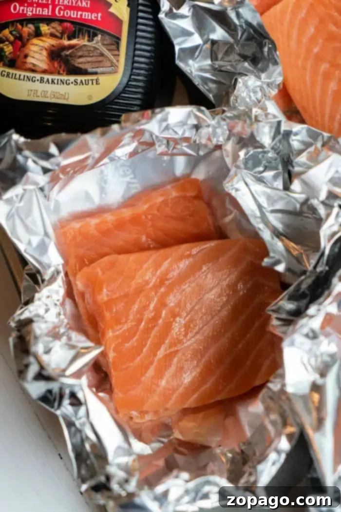 Sticky Teriyaki Salmon 4 Two fresh raw salmon fillets resting on aluminum foil, perfectly prepped for baking. A bottle of savory gourmet teriyaki sauce stands nearby, promising a delicious glaze for the oven-baked teriyaki salmon in foil.