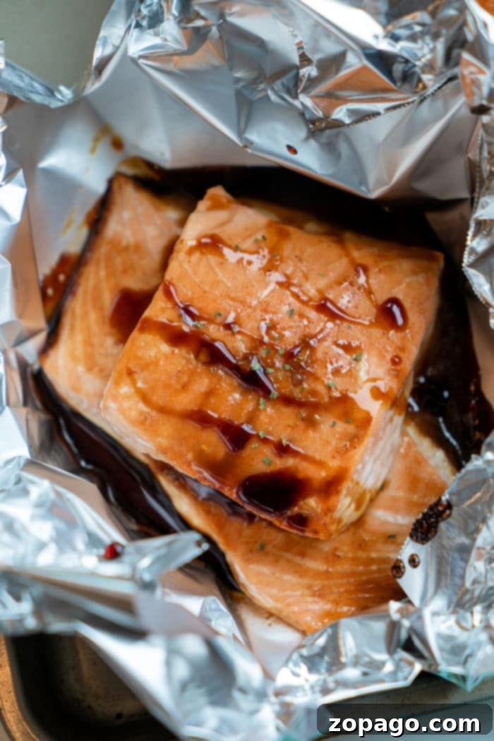 Sticky Teriyaki Salmon 8 Two perfectly cooked oven-baked teriyaki salmon fillets in foil, garnished with green onions and sesame seeds, ready to be served. The rich glaze and tender texture are clearly visible.
