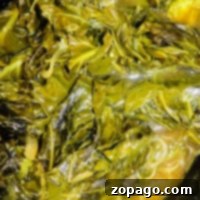 Close-up of slow cooker collard greens in a broth, showcasing their glossy texture and rich green color.