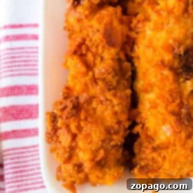 Close-up of crispy Cheese It Chicken Tenders, their orange coating glistening on a white plate, set atop a red and white striped towel.