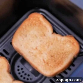 Golden brown and crisp, two slices of toast rest in a black air fryer basket, illustrating the perfection of toasting in an air fryer.