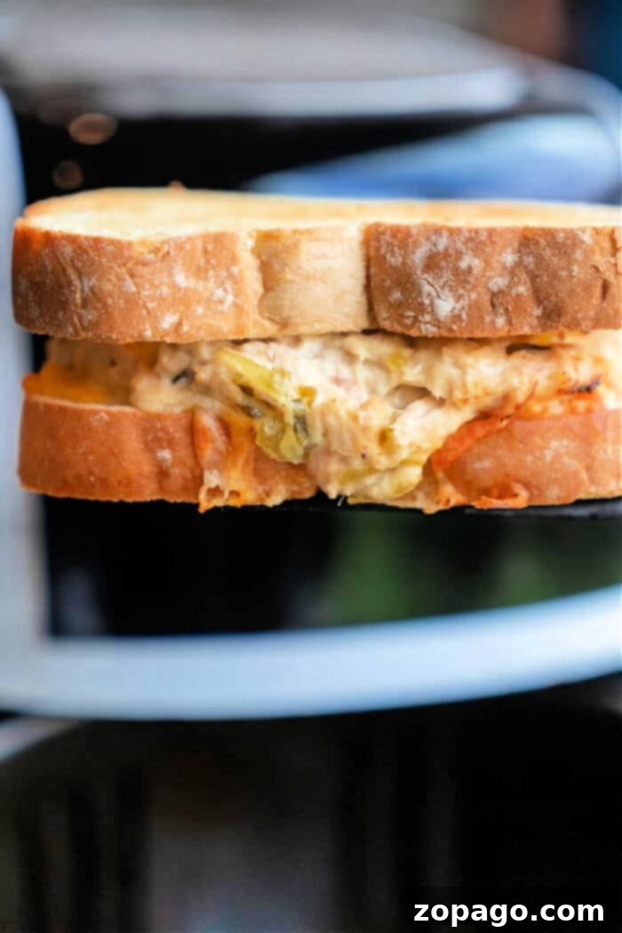 Perfectly Crisped Air Fryer Tuna Melt A close-up of a toasted air fryer tuna melt. The bread is golden brown, with the delicious filling peeking from the bitten corner.