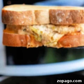 A close-up of a toasted air fryer tuna melt. The bread is golden brown, with the delicious filling peeking from the bitten corner.