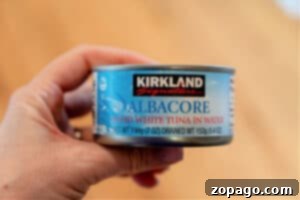 A hand holds a can of Kirkland Signature Albacore Solid White Tuna in Water, perfect for pairing with crockpot chicken dishes made from frozen breasts.