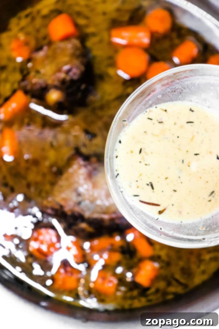 A dish with tender, cooked oxtail pieces and sliced carrots in a dark sauce is shown in a pan, reminiscent of how to cook oxtails on the stove. Above the pan, a small glass bowl holds a light creamy sauce speckled with visible herbs.
