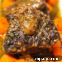 Close-up of a plate featuring braised oxtails on the stove, covered in a rich sauce and surrounded by chopped carrots. The beef is well-cooked, with a slightly charred exterior, and the carrots appear tender and flavorful.
