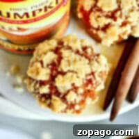 Close-up of a crumbly Libbys Pumpkin Muffin with a pumpkin can and cinnamon sticks artfully arranged on a plate.