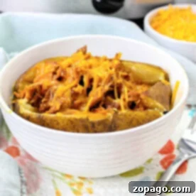 A pulled pork baked potato topped with shredded pork and melted cheese in a white bowl.