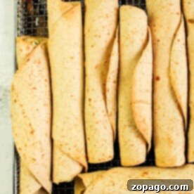 Homemade Crispy Air Fryer Chicken Taquitos 8 A tray of neatly arranged chicken taquitos rolled to perfection sits on a metal rack. The tortillas, cooked evenly in an air fryer, are light brown with visible specks.