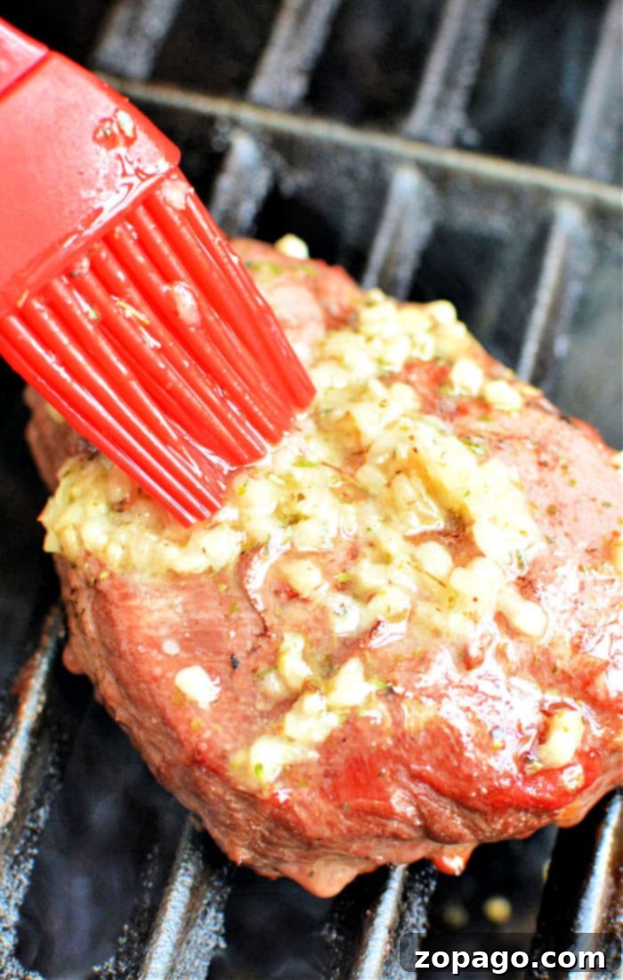 Skip the Thaw: Grill Perfect Frozen Steak 2 A red brush delicately applies garlic and herbs to a frozen steak on the grill, showcasing an essential step in the art of how to grill frozen steak to perfection.