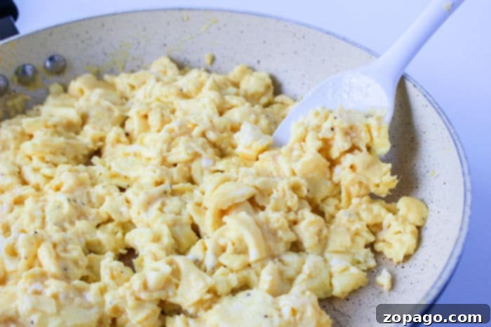 Crispy Ninja Foodi Air Fryer Breakfast Burritos 5 Scrambled eggs being stirred in a frying pan, prepared for delicious breakfast burritos