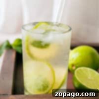 Simple Lime Refresher 6 A refreshing lime drink served in a glass with sliced lime, placed on a rustic wooden tray surrounded by whole and halved limes.