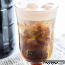 A glass of iced chocolate stout cold brew shimmers under a layer of creamy foam, elegantly perched atop a newspaper.