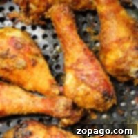 Crispy fried chicken drumsticks cooked to perfection in an air fryer, nestled in a perforated metal pan for ultimate crispiness without flour.