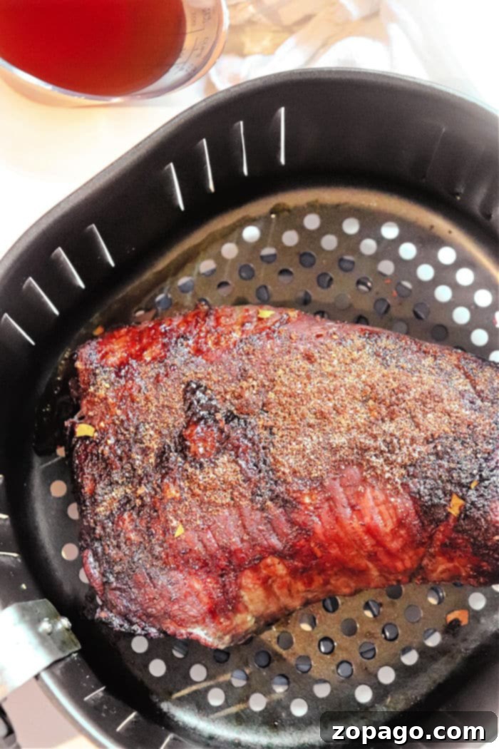 Perfectly Tender Air Fryer Brisket 6 Ninja Air Fryer Brisket cooking in an air fryer basket, showcasing the initial crisping and browning.