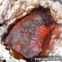 A perfectly cooked air fryer brisket resting in a pan, partially wrapped in aluminum foil, showcasing its juicy, caramelized exterior and flavorful drippings.