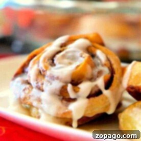 Effortless Bisquick Cinnamon Rolls 7 A plate features Bisquick Cinnamon Rolls drizzled with white icing, alongside crispy potato wedges.