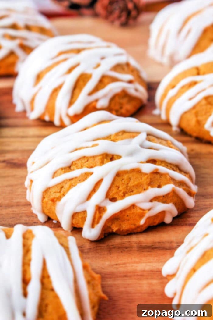 Glazed Pumpkin Spice Cookies 2 Soft, round pumpkin cookies generously drizzled with white cream cheese icing, artfully arranged on a rustic wooden background.