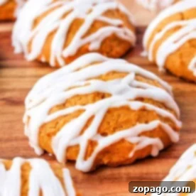 Iced Pumpkin Cookies drizzled with white icing are artfully arranged on a rustic wooden surface.